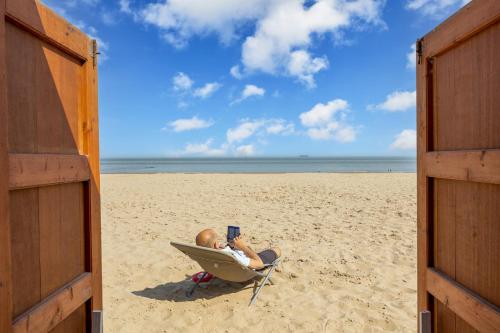 a man sitting in a chair on the beach with a laptop at Het Zoute Zand - Parkeerplaats - Wifi - Comfort - Uitzonderlijke Locatie - Ideaal voor Stellen en Gezinnen in Knokke-Heist