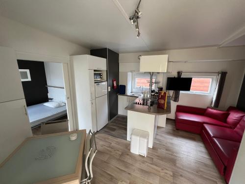un salon avec un canapé rouge et une cuisine dans l'établissement MobilHome Comfort XL (37m2) : 2 Chambres (6 personnes) - 2 SDB - Clim centralisée - TV - Terrasse balcon, à Cadenet