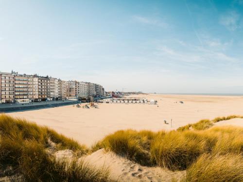 a beach with buildings and people sitting on the sand at Holiday Suites Zeebrugge in Zeebrugge