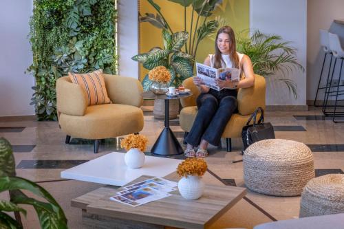 a woman sitting in a chair reading a magazine at Hotel SERHS Del Port in Barcelona