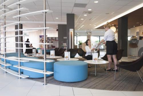 two women standing in a lobby with tables and chairs at Novotel Gdansk Centrum in Gdańsk