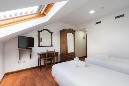 two beds in a room with a tv and a desk at Hotel La Quinta de Santillán in Chinchón