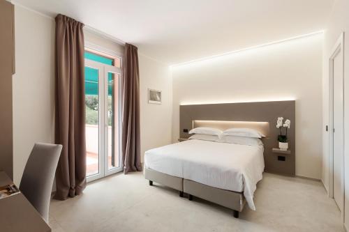a white bedroom with a bed and a large window at Hotel Villa Domizia in Porto Santo Stefano