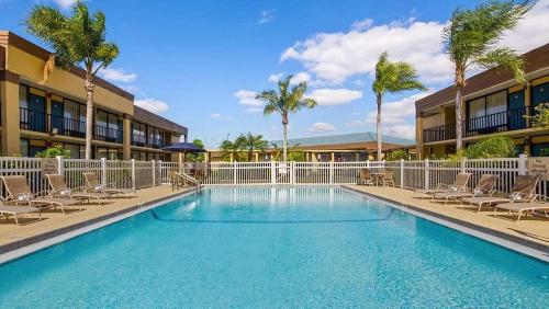 a pool with chairs and palm trees in front of a hotel at Ramada by Wyndham Cocoa in Cocoa