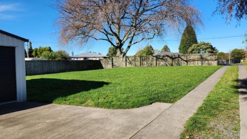 a grassy yard with a fence and a sidewalk at OakTree Entire Holiday Home, Sleeps 8 to12 in Rotorua