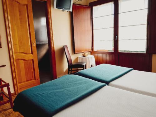 a bedroom with two beds and a chair and a table at Hotel Vitorio in Cudillero