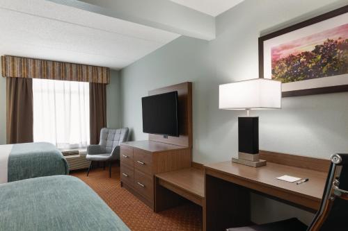 a hotel room with a bed and a desk with a television at Wingate by Wyndham Louisville East in Louisville