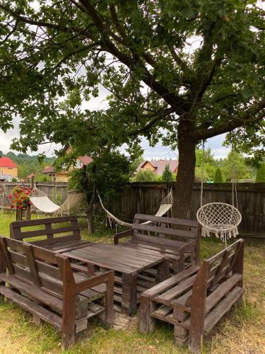 three wooden benches sitting under a tree with a hammock at Kwatera Pod Bukowa Gora in Zwierzyniec