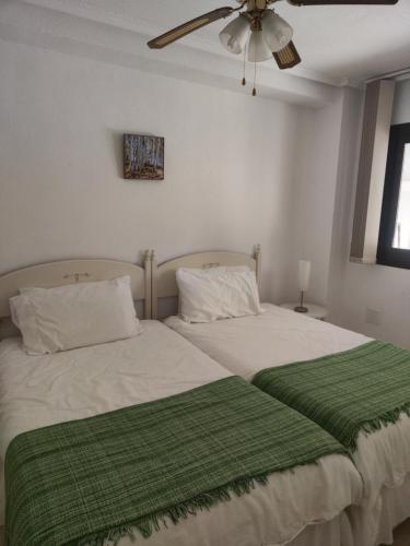 a bedroom with two beds with green sheets and a ceiling fan at Casa Marius in La Mata