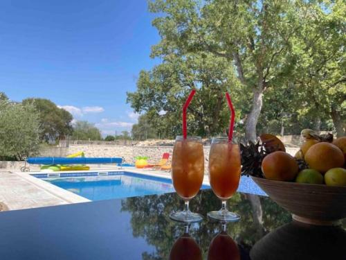 two glasses of juice and a bowl of fruit next to a pool at Villa Idylee in Drniš