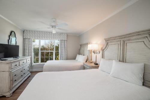 a white bedroom with two beds and a television at Litchfield Beach & Golf Resort in Pawleys Island