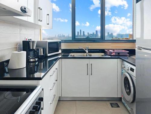 Una cocina con gabinetes blancos y un fregadero y una ventana. en Panoramic Luxury Apartment, en Abu Dabi
