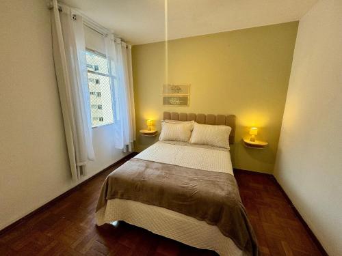 a bedroom with a bed with two lamps on two tables at Apartamento ao lado da Praça do Suspiro com vaga de garagem in Nova Friburgo