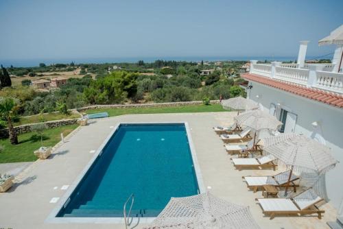 a pool with chairs and umbrellas next to a building at Pantheon Villa Svoronata in Svoronata