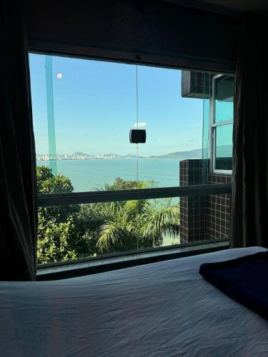 a bedroom with a large window looking out at the ocean at Apartamento Sunset House Porchat in São Vicente