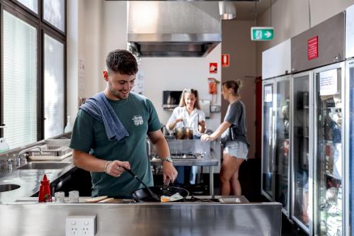 a man preparing food in a kitchen with people in the background at Wake Up! Sydney Central in Sydney