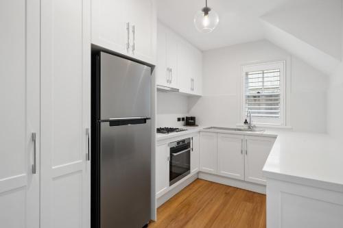 a kitchen with white cabinets and a black refrigerator at Harbour View Terrace House In The Heart Of The Rocks in Sydney