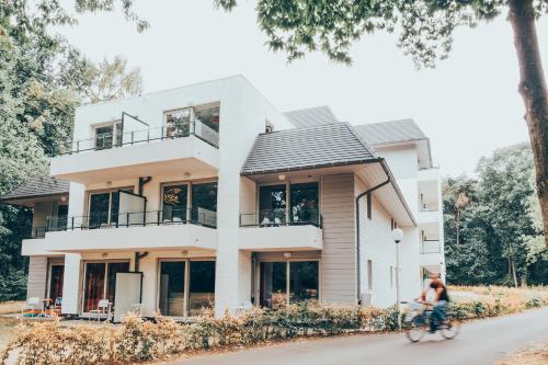 a woman riding a bike in front of a house at Green Resort Limburg in Houthalen-Helchteren