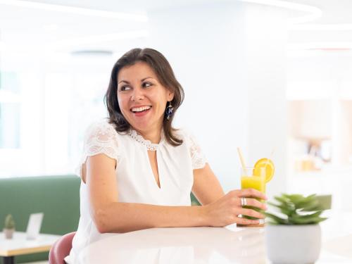 a woman sitting at a table with a glass of orange juice at Novotel Suites Montpellier Antigone in Montpellier