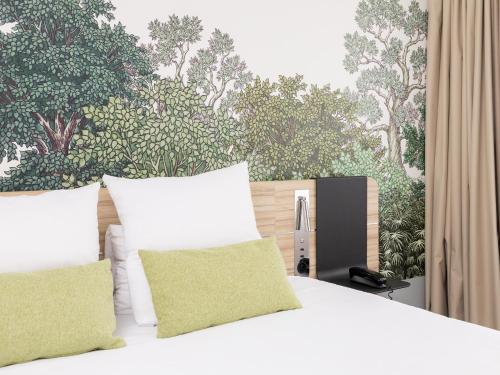 a bed with white pillows and a wall with trees at Novotel Suites Montpellier Antigone in Montpellier