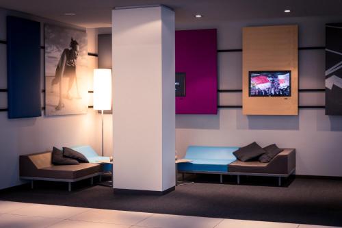 a lobby with two couches and a tv on a wall at Lindner Hotel Frankfurt Sportpark, part of JdV by Hyatt in Frankfurt/Main