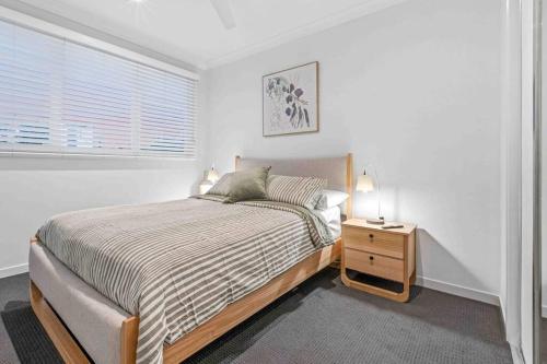 a white bedroom with a bed and a night stand at Redcliffe CBD Family Beach House in Redcliffe