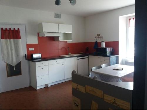 a kitchen with white cabinets and a red wall at Gîtes du Café de la Poste in Le Buisson