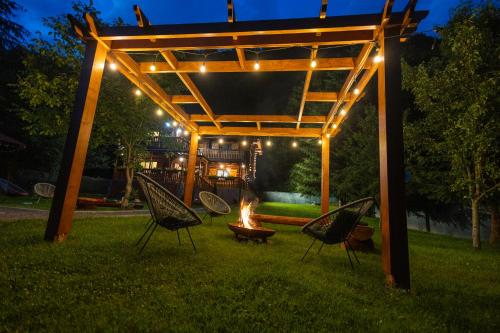 a pergola with chairs and a fire in the grass at Casa Bucuriei - Plaiul Foii, Zărnești in Zărneşti