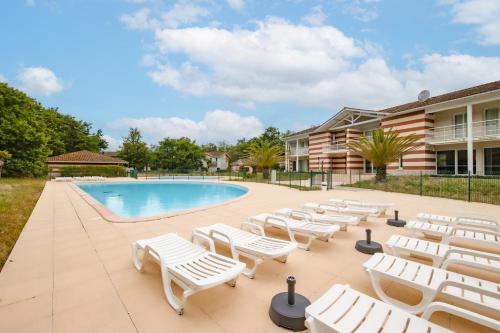un groupe de chaises longues et une piscine dans l'établissement Maison de ville Domaine des sables, à Soulac-sur-Mer