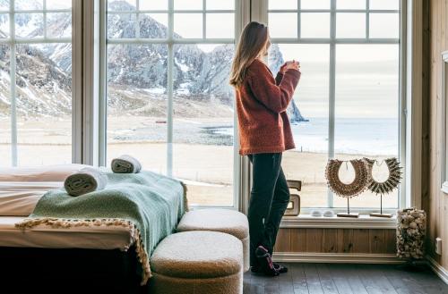 a woman standing in a window looking out at the snow at Unstad Arctic Resort in Unstad