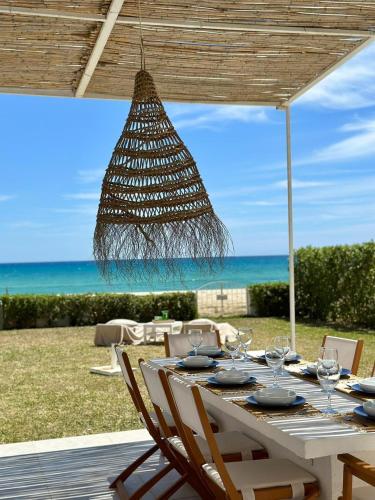 a white table with chairs and a chandelier and the ocean at Beach house Hammamet in Hammamet Nord