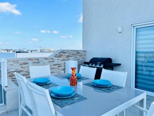 a dining table with white chairs and blue dishes on it at Poseidon Court Penthouse SUPERIOR in St. Paul's Bay
