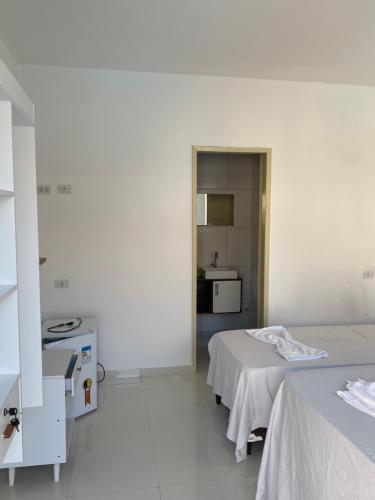 a white room with two beds and a kitchen at Pousada Good Vibes in Japaratinga