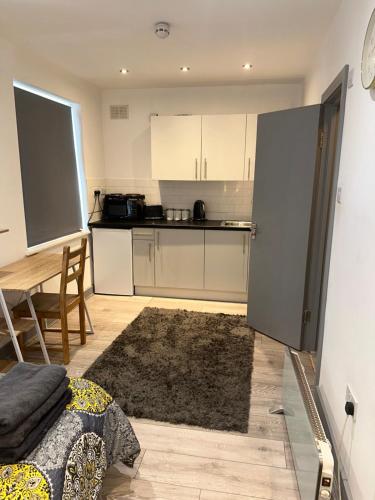 a kitchen with white cabinets and a table with a rug at Modern studio flat in Romford in Havering atte Bower
