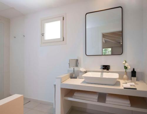 a white bathroom with a sink and a mirror at Baia Di Chia Resort Sardinia, Curio Collection By Hilton in Chia