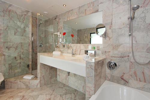 a bathroom with a sink and a shower and a tub at ARCOTEL Nike Linz in Linz