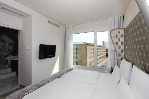 a white bedroom with a large bed and a window at ARCOTEL John F Berlin in Berlin