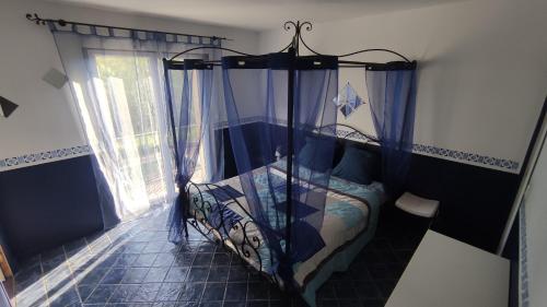- une chambre avec un lit doté de rideaux bleus et d'une fenêtre dans l'établissement Domaine de Bernassa - Intimité et calme au coeur de 20 hectares de nature, à Saint-Hilaire-de-Lusignan