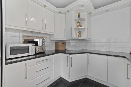 a white kitchen with white cabinets and a microwave at 3 Bedroom Bungalow Sunningdale Lodge Ascot Races in Sunningdale