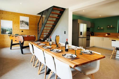 une longue table en bois avec des chaises blanches et un escalier dans l'établissement Chalet Mont-Lac à 100m du Lac, à Gérardmer