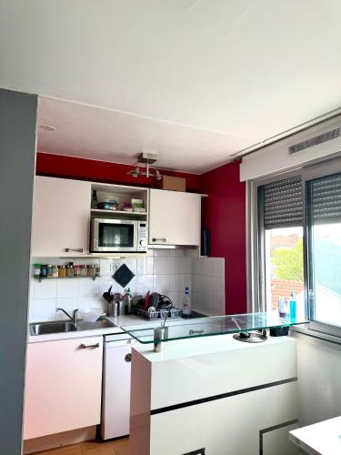 une cuisine avec des placards blancs et un mur rouge dans l'établissement Charmant studio à 7min de Paris, à Clichy