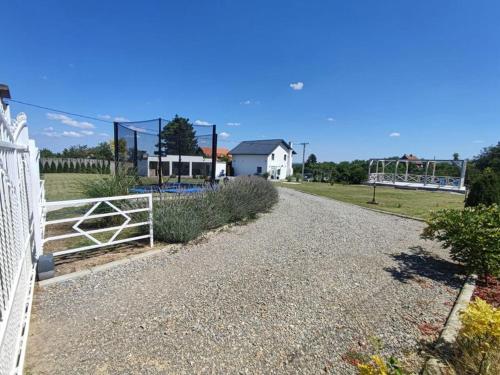 a gravel driveway with a white fence and a field at Vila La hacienda in Beška