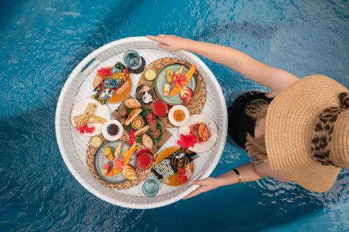 a woman holding a plate of food next to a pool at Xanadu Luxury Villas & Retreat Zanzibar in Bwejuu
