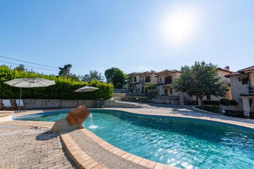 a swimming pool with an umbrella and a fountain at Lous House in Agia Paraskevi