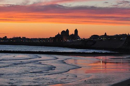 a sunset over a beach with a city in the background at Muy cerca de playa in Cádiz