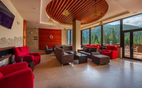 a living room with red chairs and tables and windows at Wellness Hotel Repiska in Demanovska Dolina