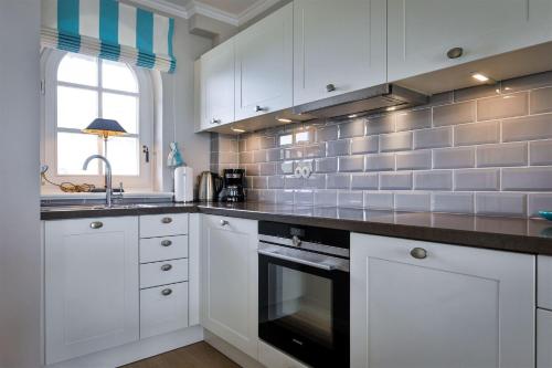 a kitchen with white cabinets and a black oven at Heefkant Haus Heefkant,HK 02 in Rantum