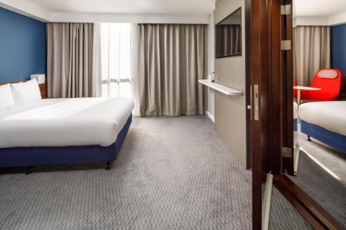 a hotel room with two beds and a red chair at Holiday Inn Express London - ExCel by IHG in London
