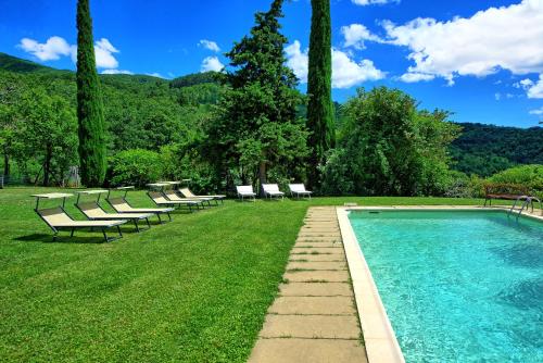 a swimming pool with chaises and chairs in a park at Poggiolino by PosarelliVillas in Chitignano
