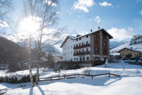 a building in the snow with the sun behind it at Hotel & Restaurant Saint Nicolas Gran Paradiso in Saint Nicolas